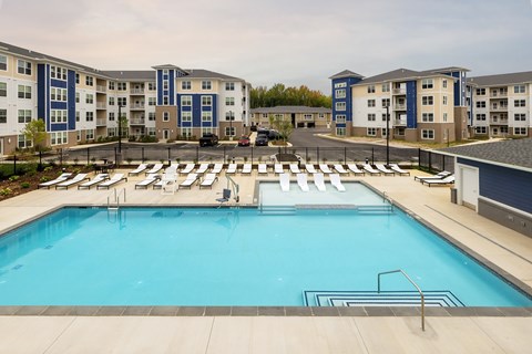 A large swimming pool surrounded by sun loungers and apartment buildings.