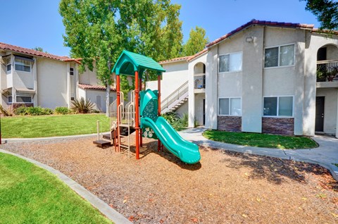 A playground with a green slide in front of apartment buildings.