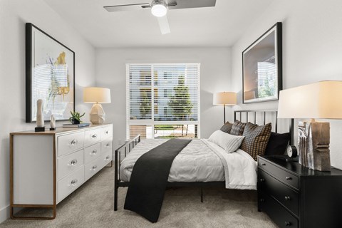 Studios in Sacramento, CA - The Eisley - Bedroom with Plush Carpeting, Ceiling Fan, a Large Bed with Black Nightstand, and Oversized Window