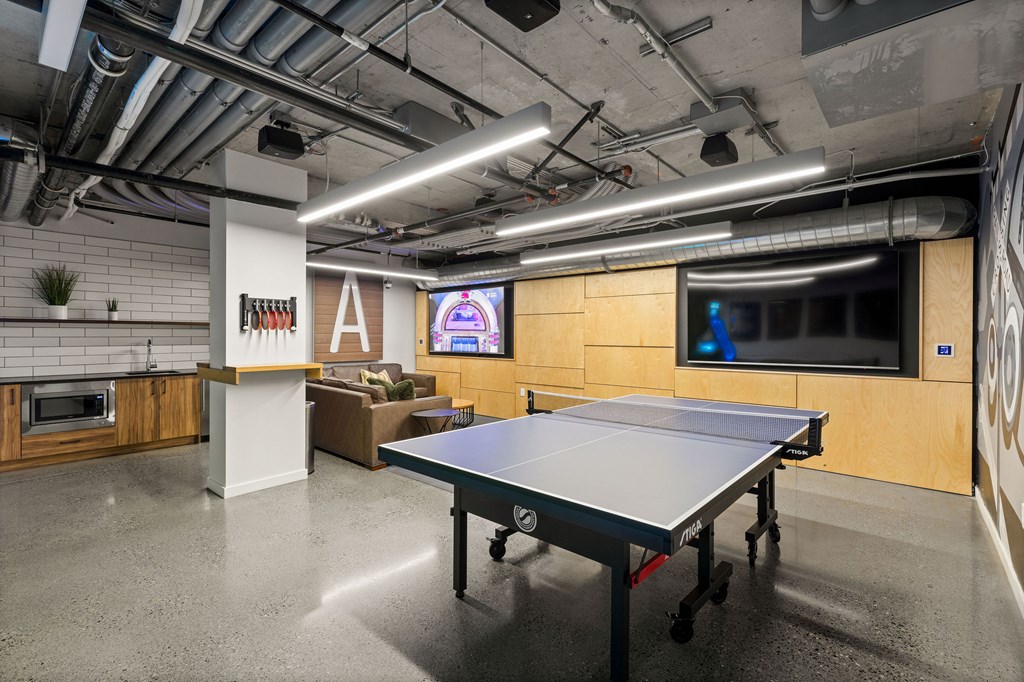 A ping pong table is in the middle of a room with a TV and a bar.