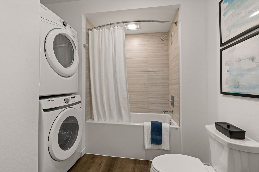A white washing machine is in a small bathroom with a toilet and a bathtub.