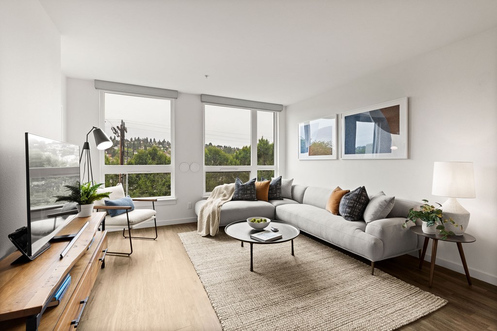 A modern living room with a grey sofa, a coffee table, and a large window overlooking a green landscape.