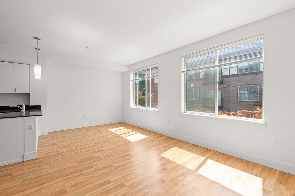 A room with wooden floors and a kitchen area with white cabinets.