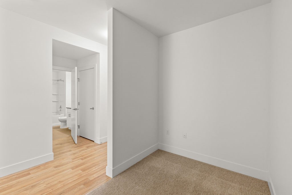 A white room with a carpet and a doorway leading to another room.