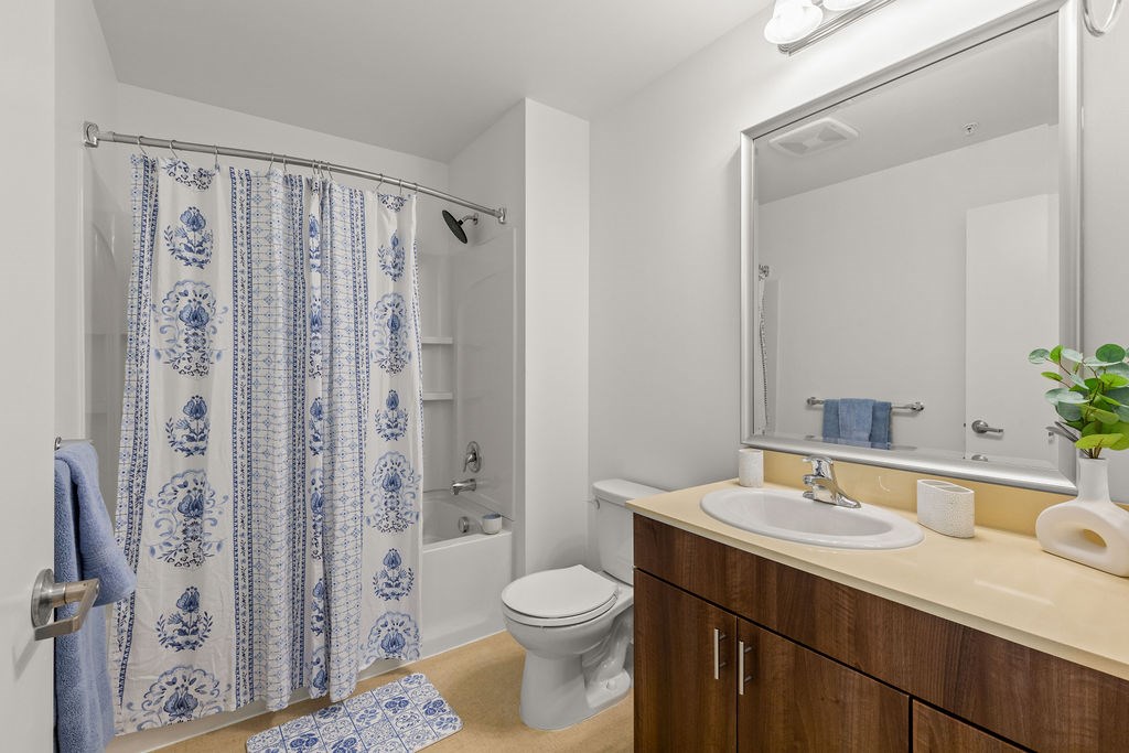 A bathroom with a white toilet, a sink, a mirror, and a shower with a blue and white shower curtain.