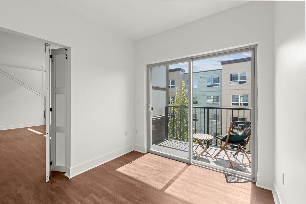 A room with a sliding glass door leading to a balcony with a chair and a table.