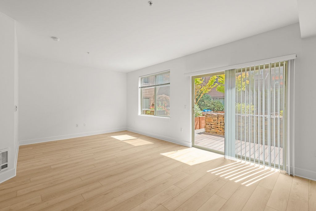 A room with wooden flooring and a window with a view of a backyard.