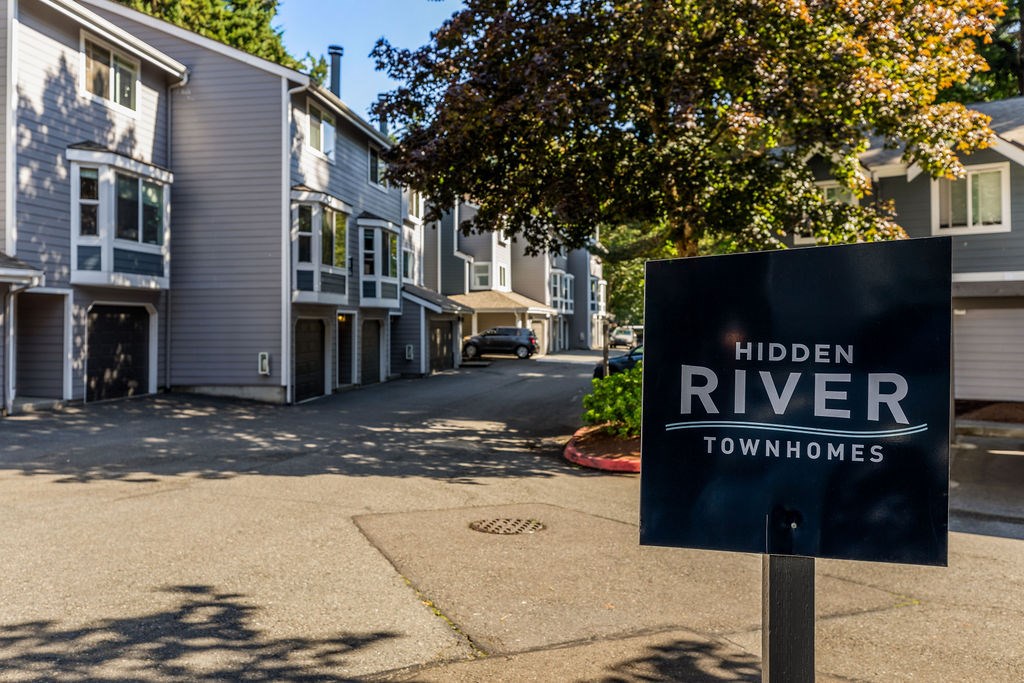 A sign for Hidden River Townhomes stands in front of a building.