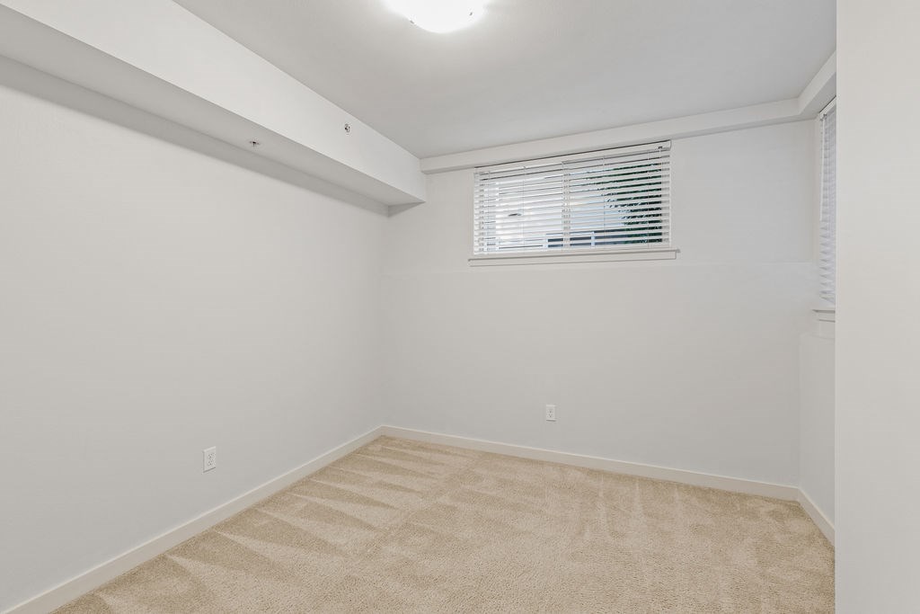 A room with a beige carpet and a window with blinds.
