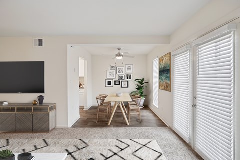 A modern living room with a flat screen TV, a dining table with chairs, and a rug on the floor.