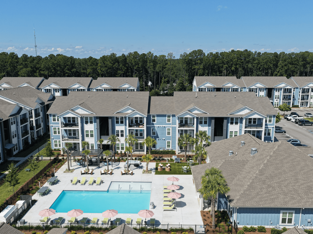 A large apartment complex with a pool and a patio with chairs and umbrellas.