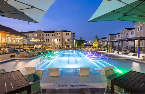 a swimming pool at night with tables and chairs around it