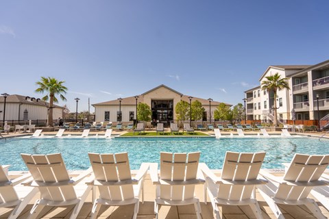 A pool with white chairs and a building in the background.