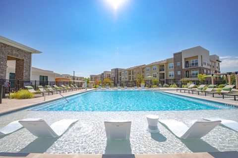 a swimming pool with chairs and an apartment building in the background