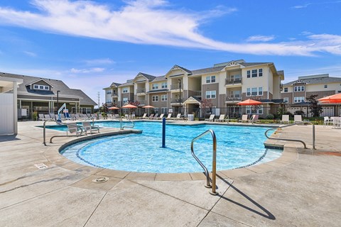 A swimming pool surrounded by lounge chairs and umbrellas in front of apartment buildings.