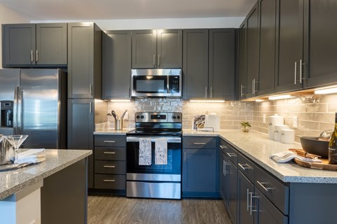 A modern kitchen with dark grey cabinets and stainless steel appliances.