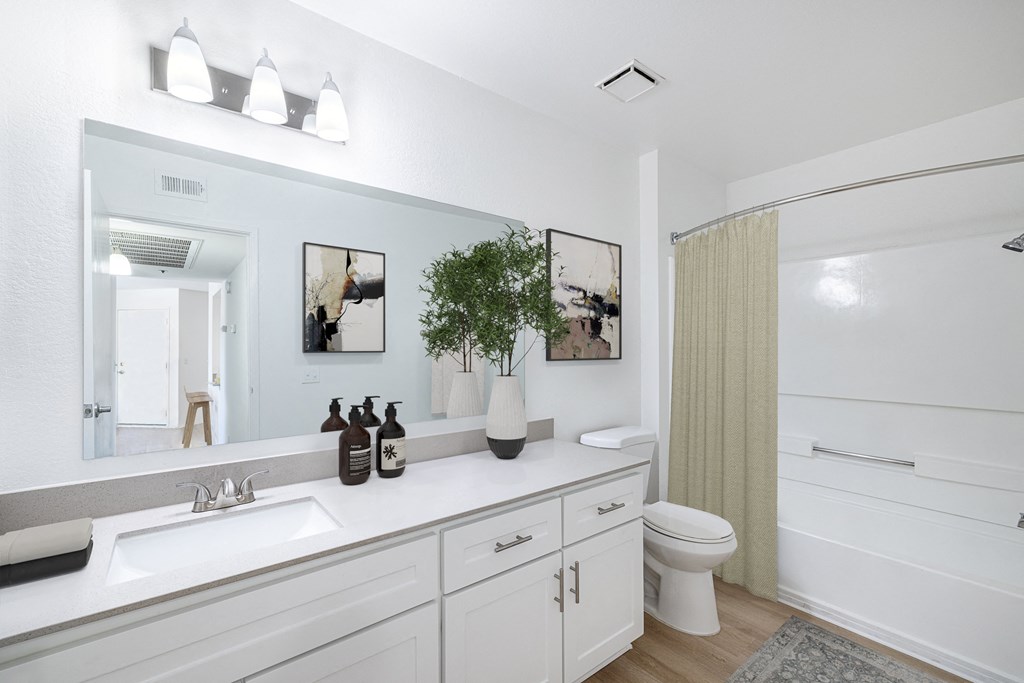 a bathroom with white cabinets and a white toilet next to a white bathtub with a shower