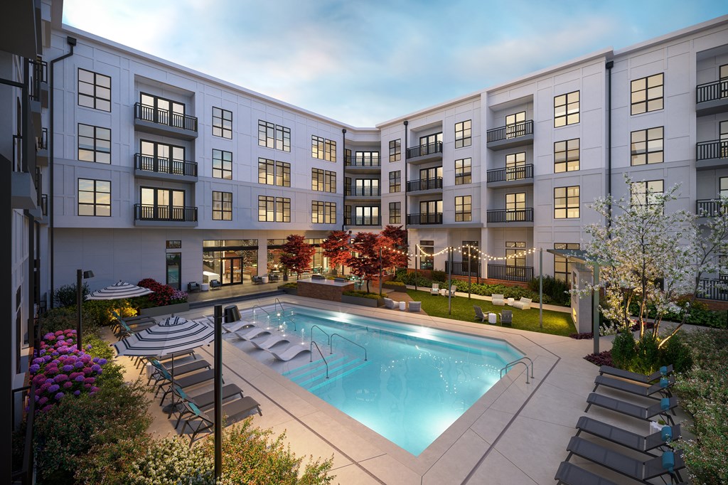 A swimming pool is surrounded by lounge chairs and trees in front of apartment buildings.