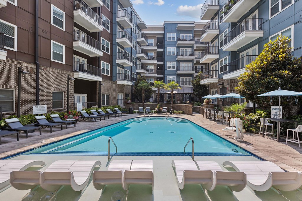 an outdoor swimming pool with lounge chairs and umbrellas in front of an apartment building