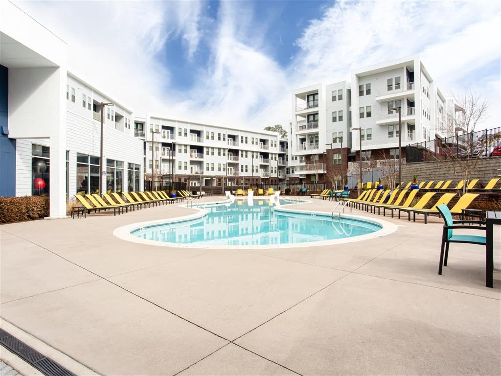 a resort style pool with yellow lounge chairs and buildings in the background
