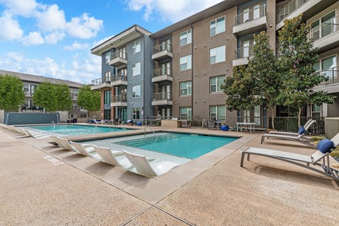 A large apartment complex with a pool and sun loungers.