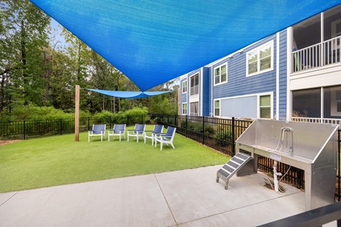 A blue shade structure is over a patio with chairs and a hot tub.