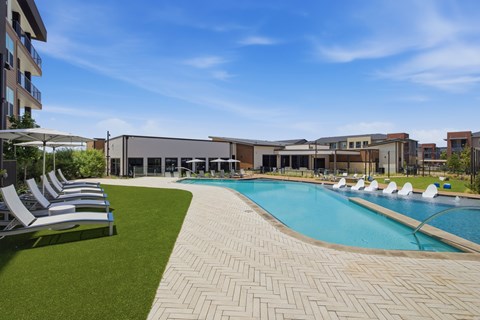 A large outdoor swimming pool surrounded by lounge chairs and buildings.