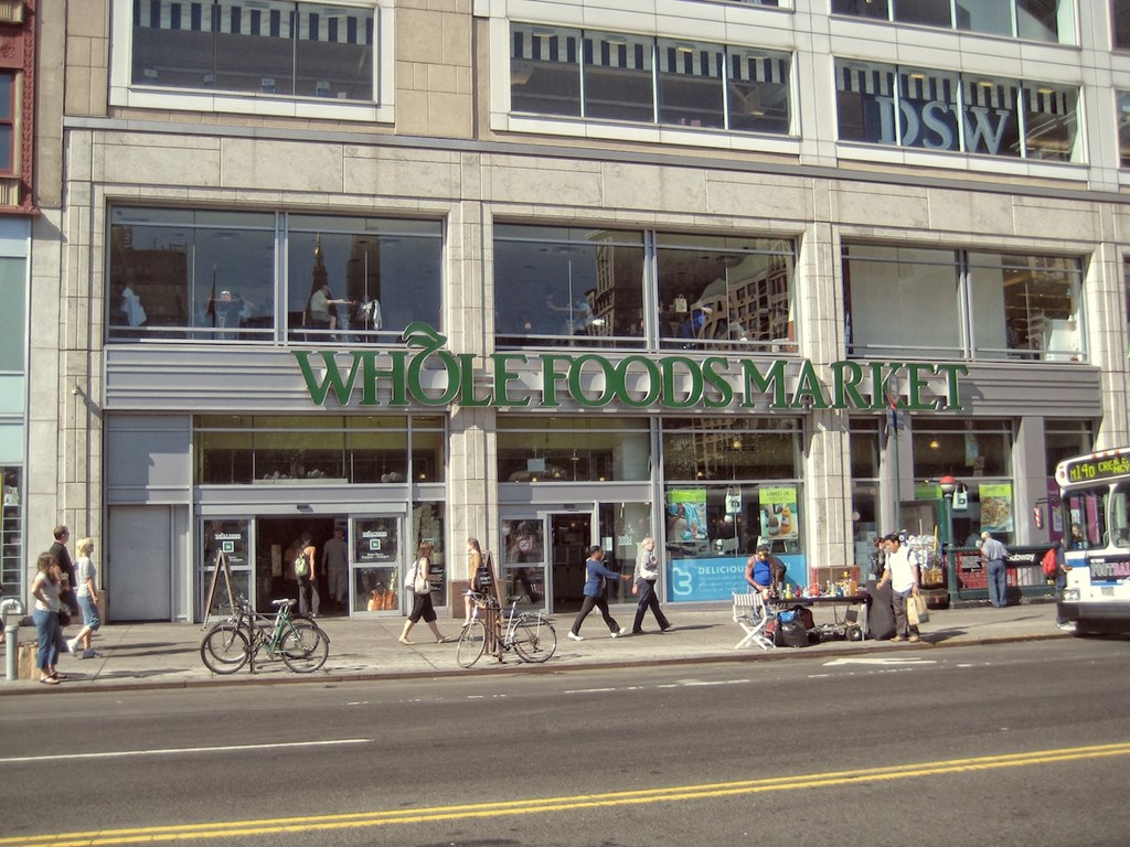 people walking on the sidewalk in front of a building with the words whole foods market on it