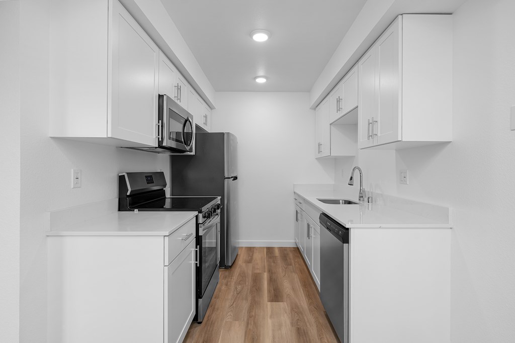 A black and white photo of a kitchen with white cabinets and black appliances.