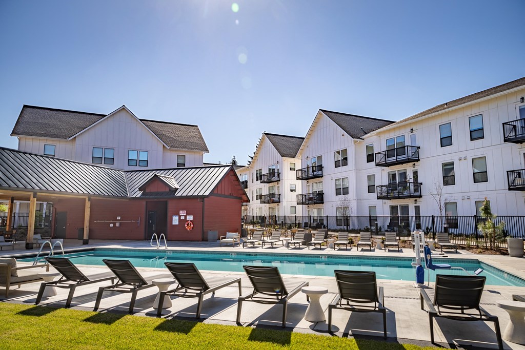 a swimming pool with lounge chairs in front of apartment buildings at The Farmstead, Vancouver Washington