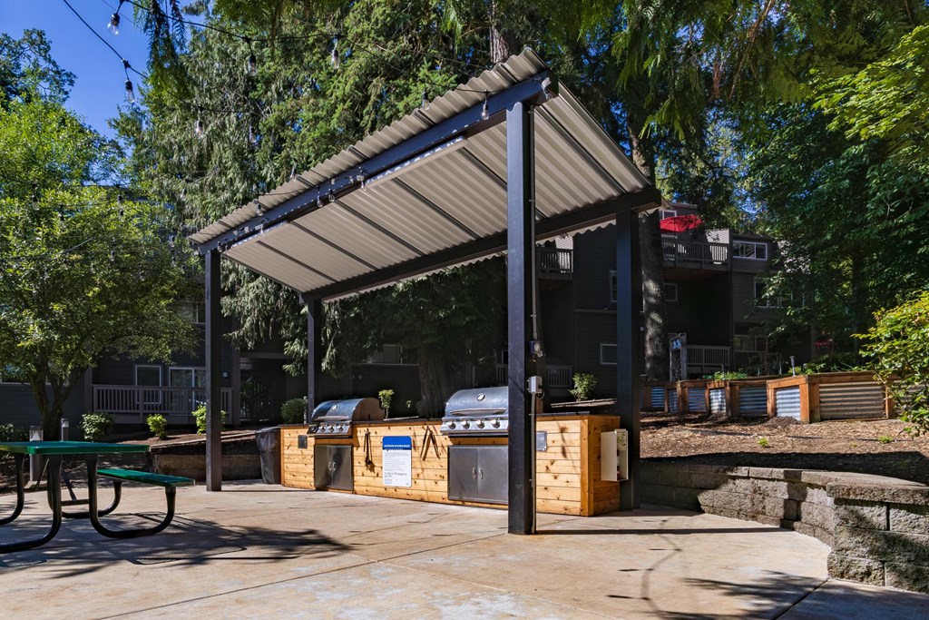 A covered picnic area with a grill and a table.