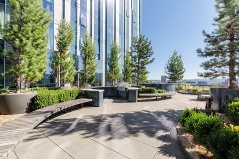 A modern courtyard with a glass building in the background and trees around the area.
