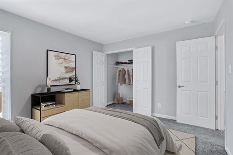 A bedroom with a large bed and a closet with clothes hanging inside.