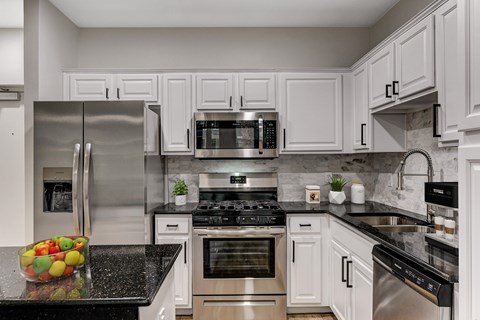 A kitchen with white cabinets and black countertops.
