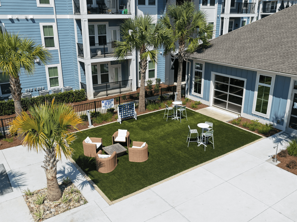 A patio area with a table and chairs surrounded by a grassy area and palm trees.
