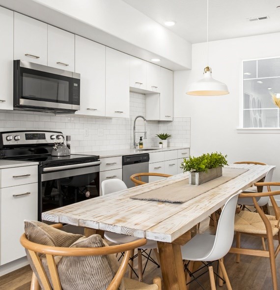 A modern kitchen with a wooden table and white chairs.