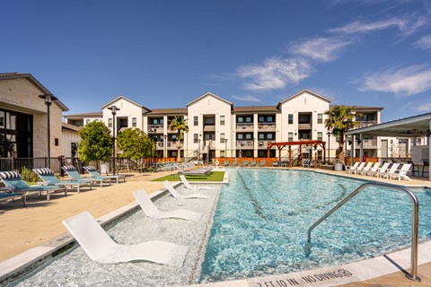 A large swimming pool with lounge chairs in front of apartment buildings.