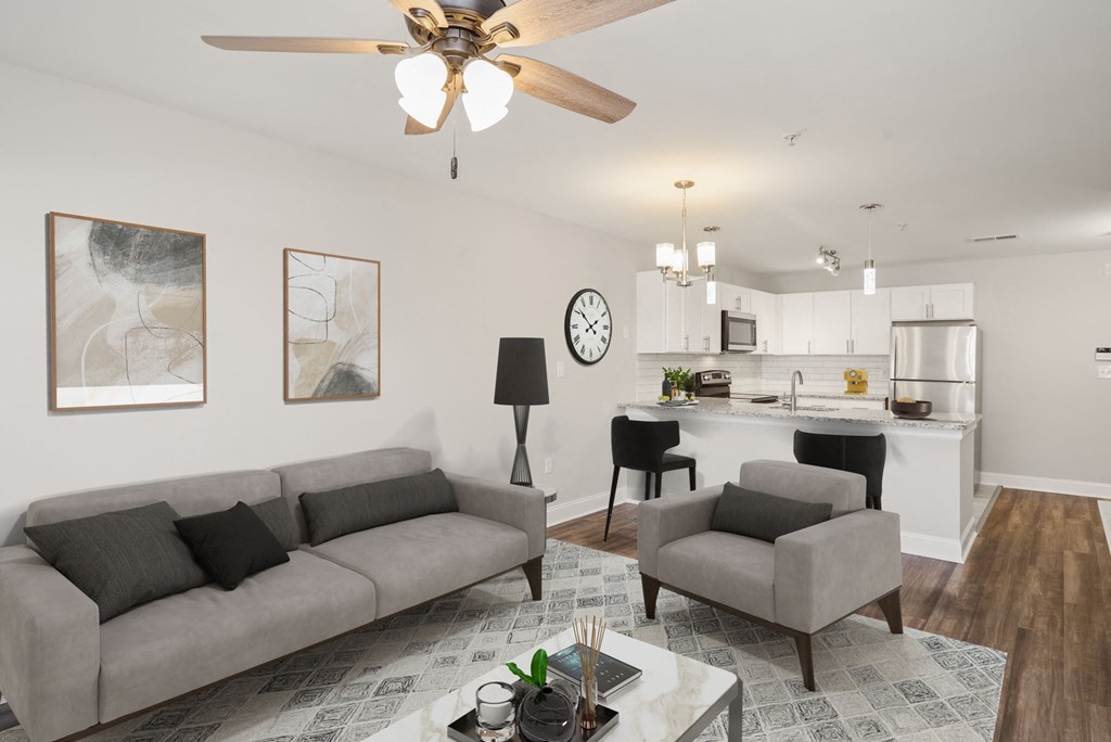 a living room with a couch and two chairs in front of a kitchen with a breakfast bar