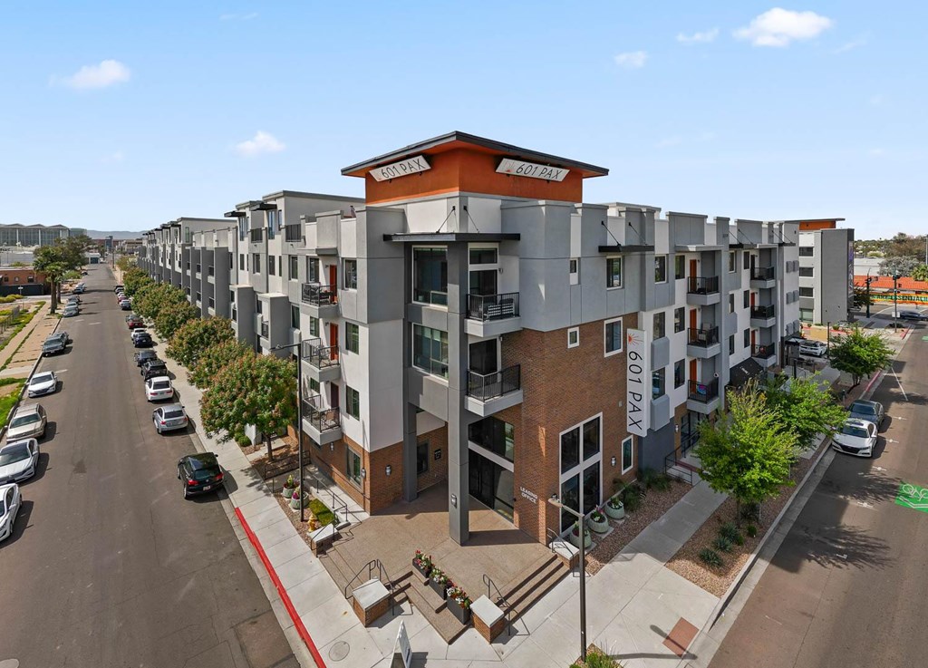 A street view of a residential area with apartment buildings and cars parked on the side of the road.