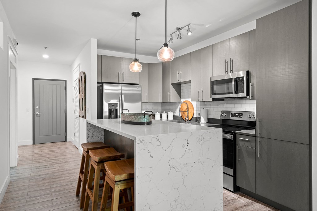 Kitchen with grey cabinets, waterfall island with stools, French door fridge