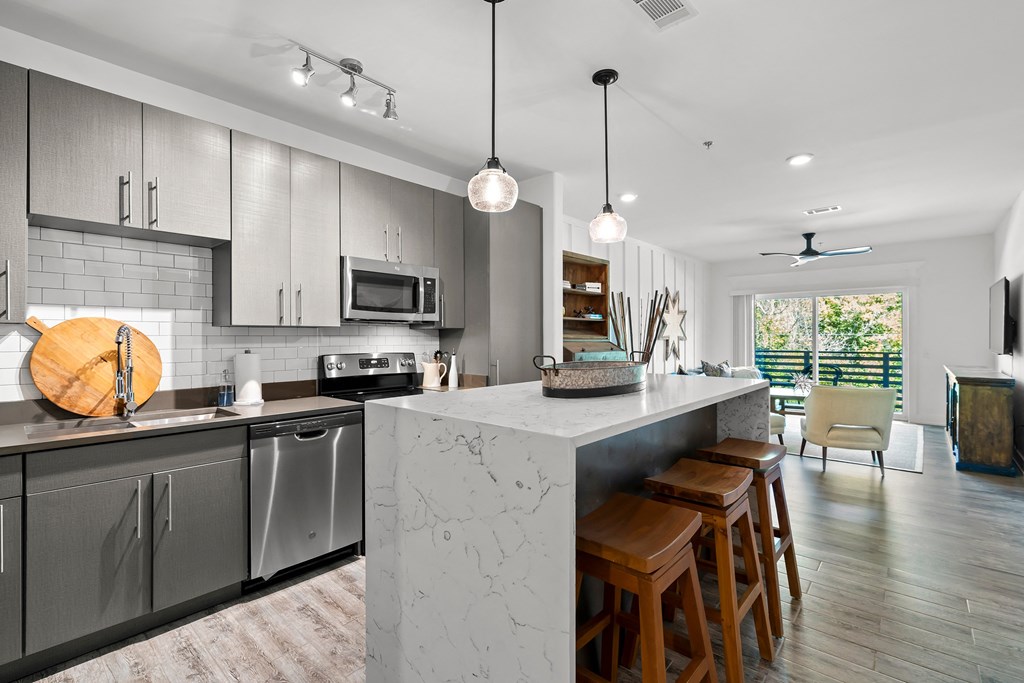 Kitchen with grey cabinets, waterfall island with stools, open to living room
