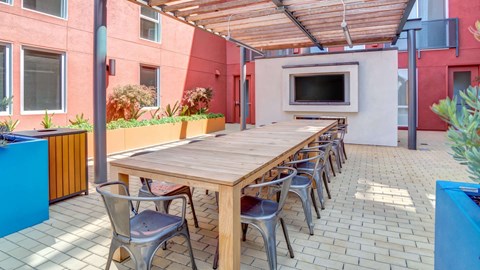 A long wooden table is surrounded by chairs on a patio.