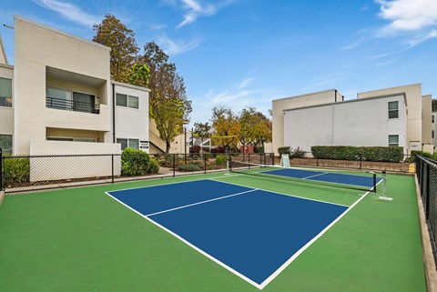 A tennis court is surrounded by apartment buildings.