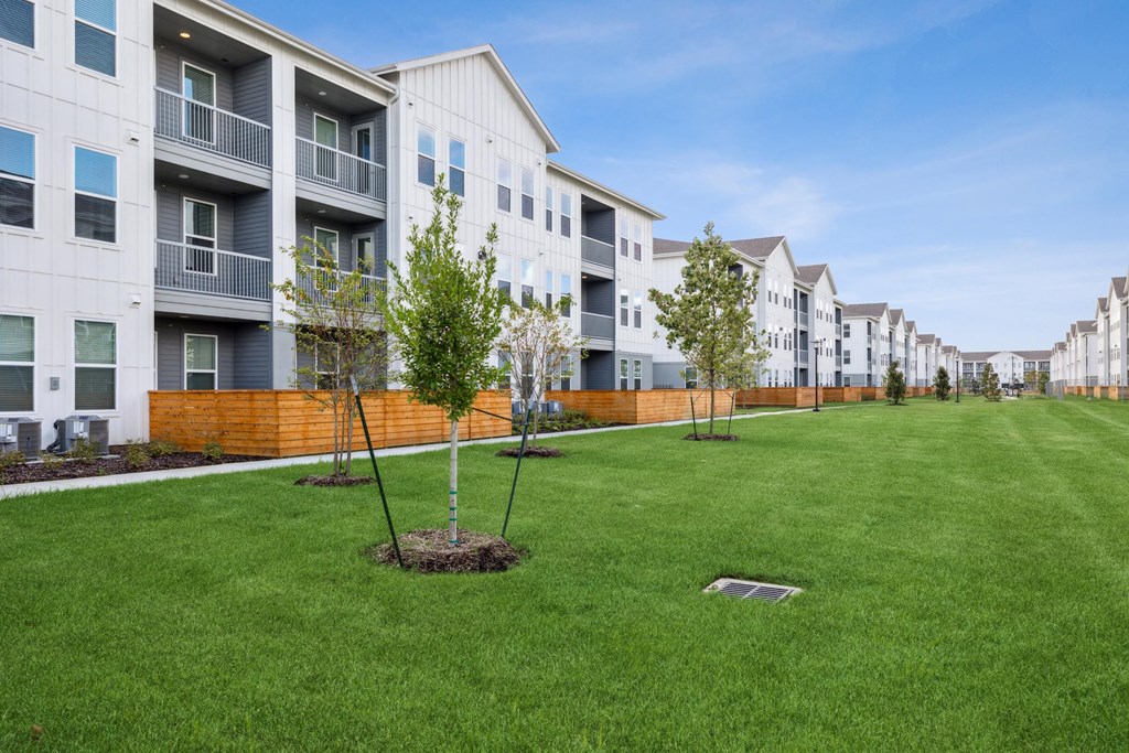 a green lawn with trees in front of an apartment building
