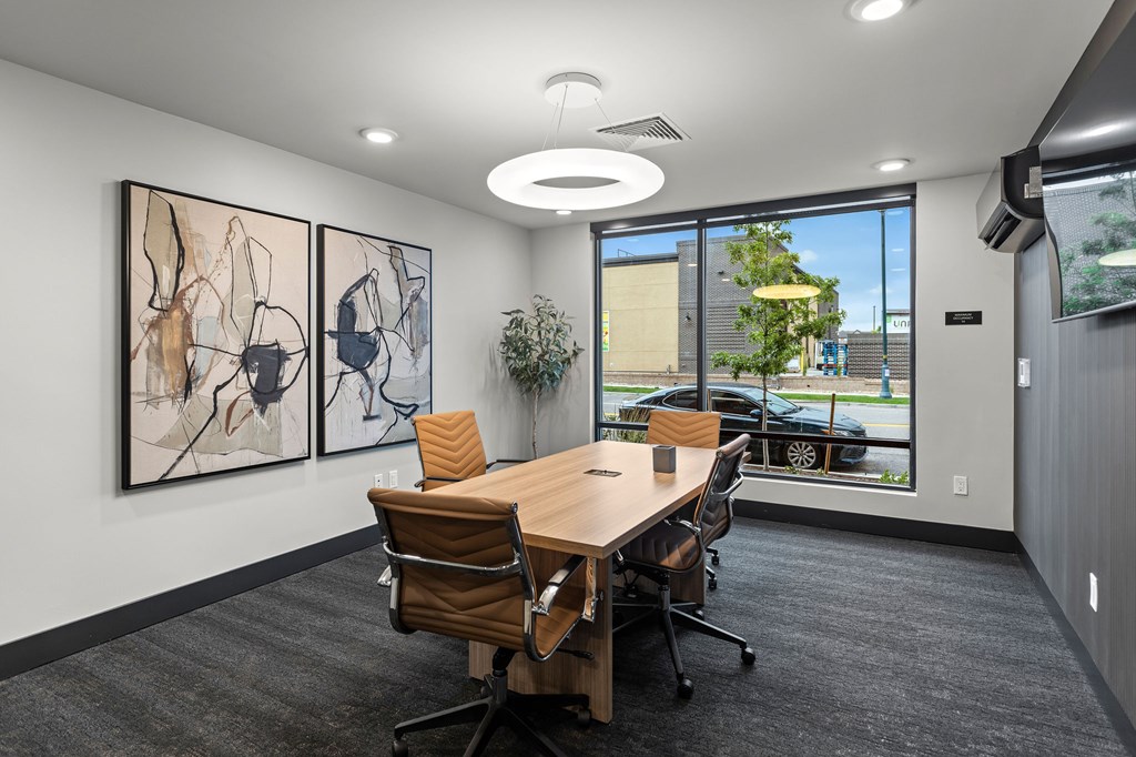 A conference room with a long table and chairs, a plant, and two abstract paintings on the wall.