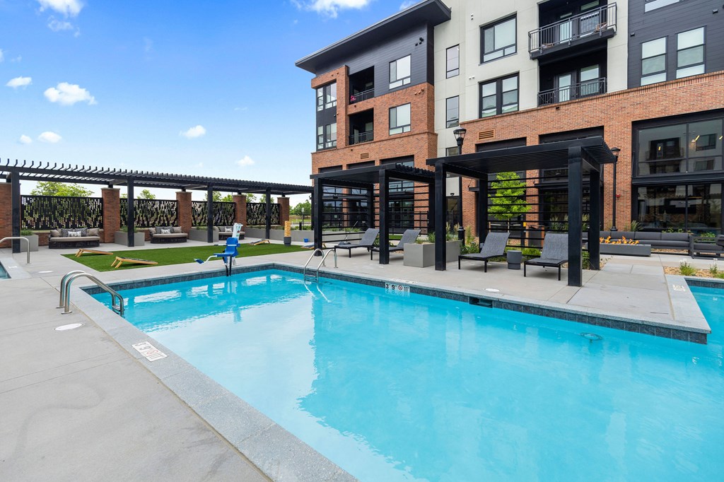 A swimming pool in front of a building with a person sitting on a chair.
