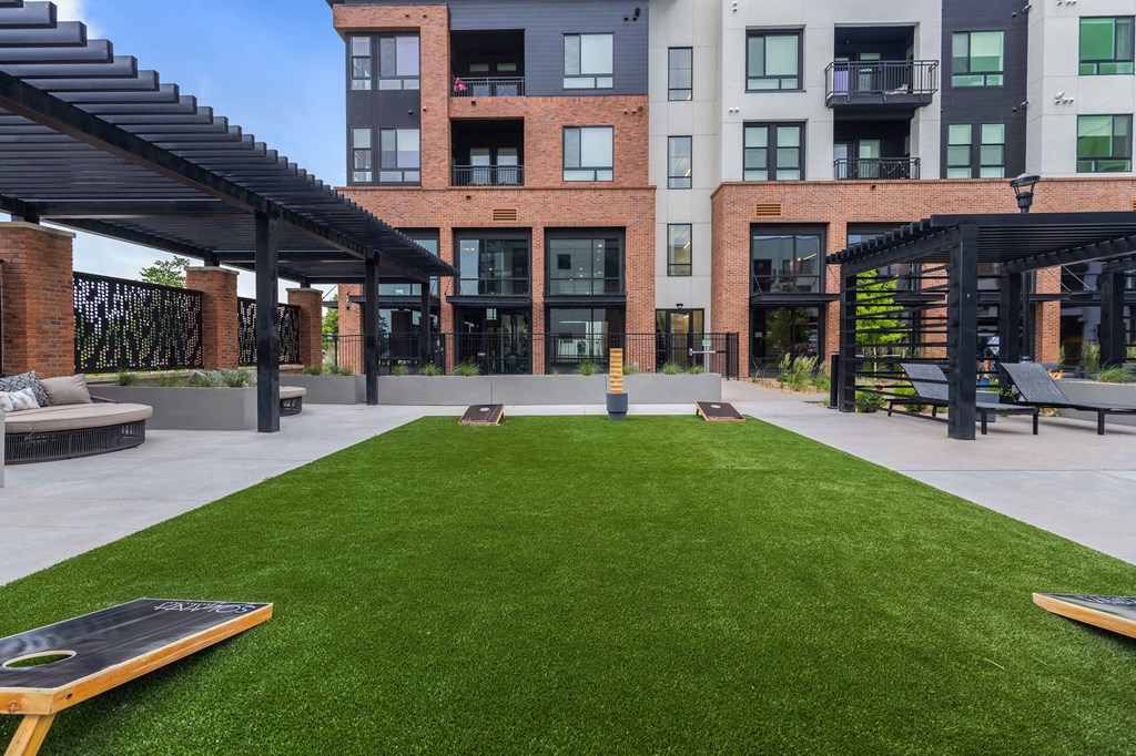 A grassy area in front of a building with a black pergola.