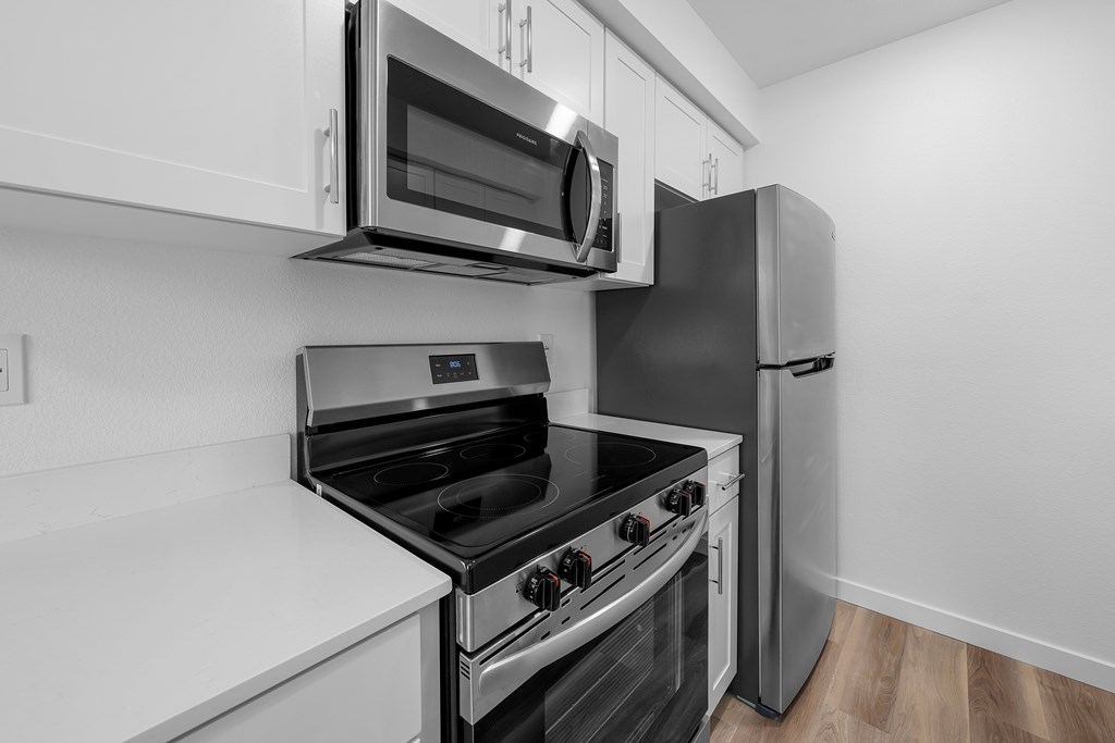 A black and white photo of a kitchen with a stove, oven, microwave, and refrigerator.