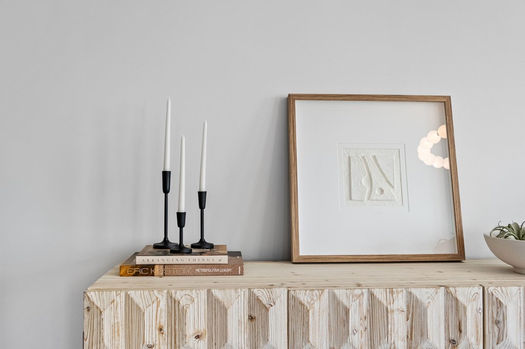 A wooden table with a framed picture, candles, and a plant on it.