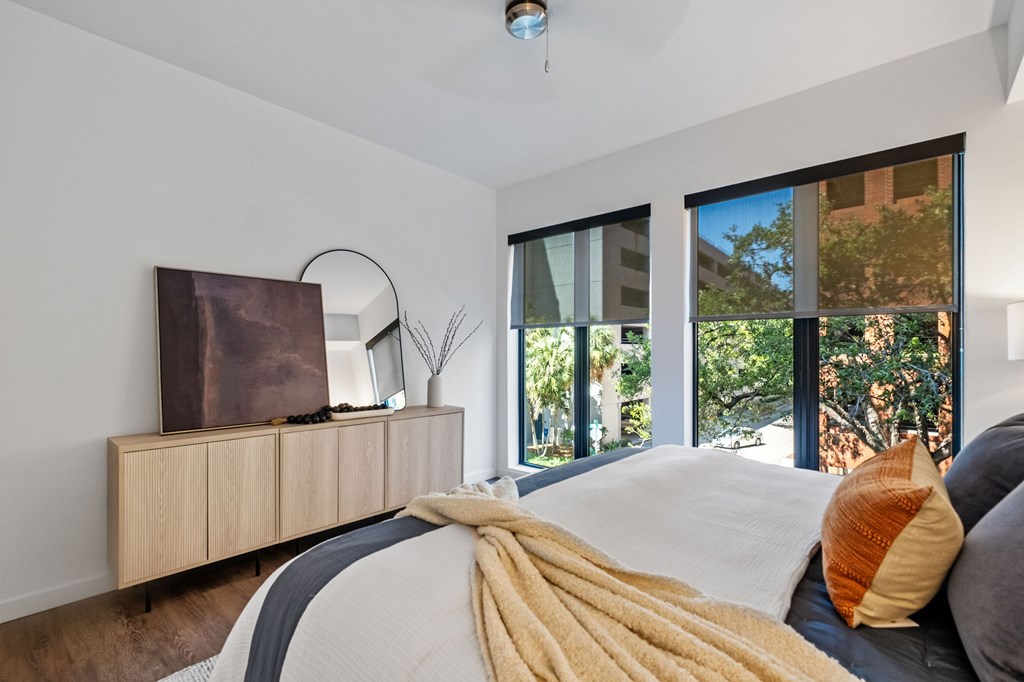 A bedroom with a bed covered in a white comforter and a wooden dresser with a mirror and a lamp on top.